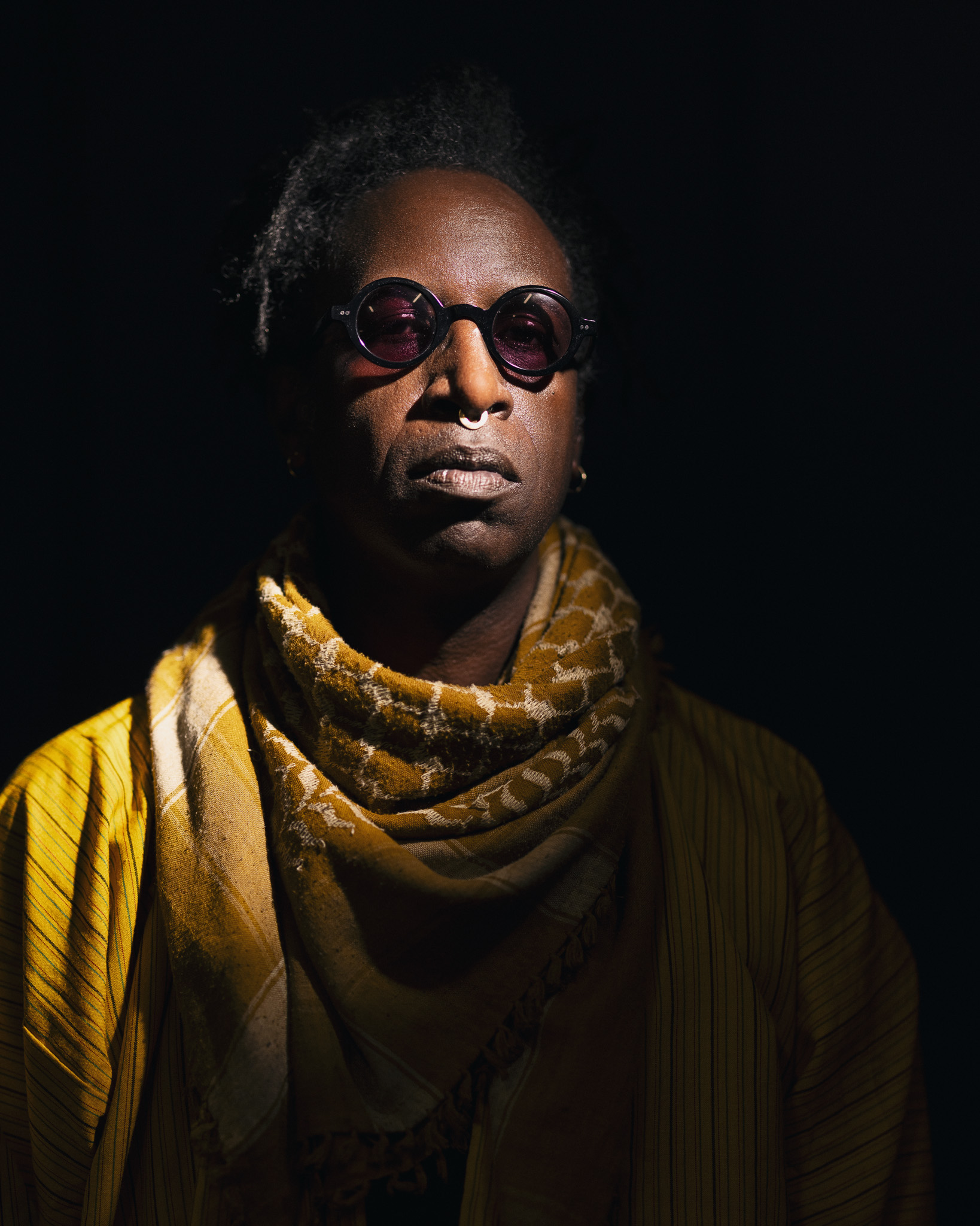 A portrait of Saul Williams. The background is black. A light shines on Saul Williams from the top right of the photo.